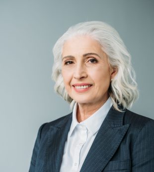 portrait of smiling senior businesswoman in suit isolated on grey